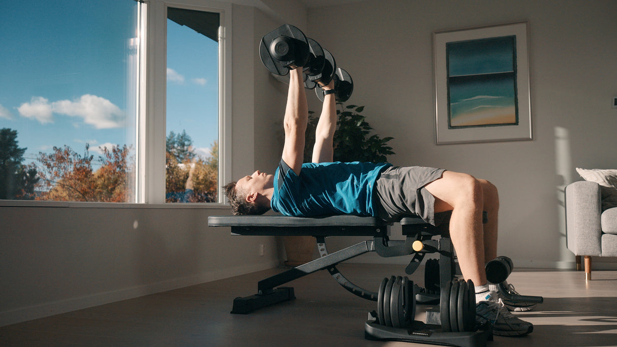 Person exercising with dumbbells on a weight bench in a home setting.