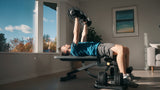 Person exercising with dumbbells on a weight bench in a home setting.